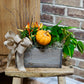 Decorative arrangement with pumpkins and greenery on a wooden stool against a brick wall.