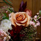 Close-up of a bouquet with a prominent peach rose against a blurred wooden background