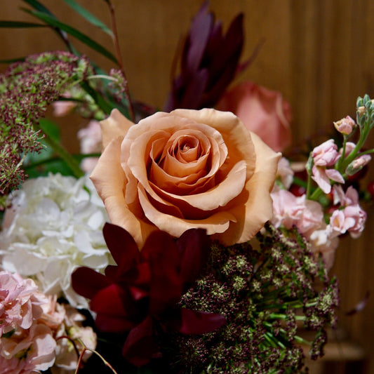 Close-up of a bouquet with a prominent peach rose against a blurred wooden background