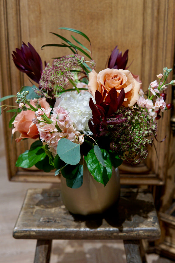 Floral arrangement in a vase on a wooden stool with a wooden panel background