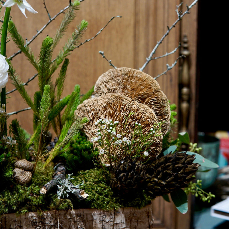 Decorative arrangement with greenery, mushrooms, and flowers against a wooden background