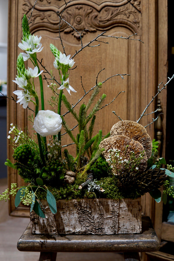 Floral arrangement with white flowers and greenery in a wooden box against a wooden door.