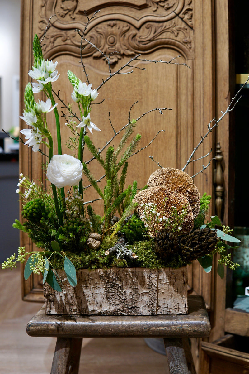 Floral arrangement in a wooden box on a rustic wooden stool with a decorative wooden panel in the background.