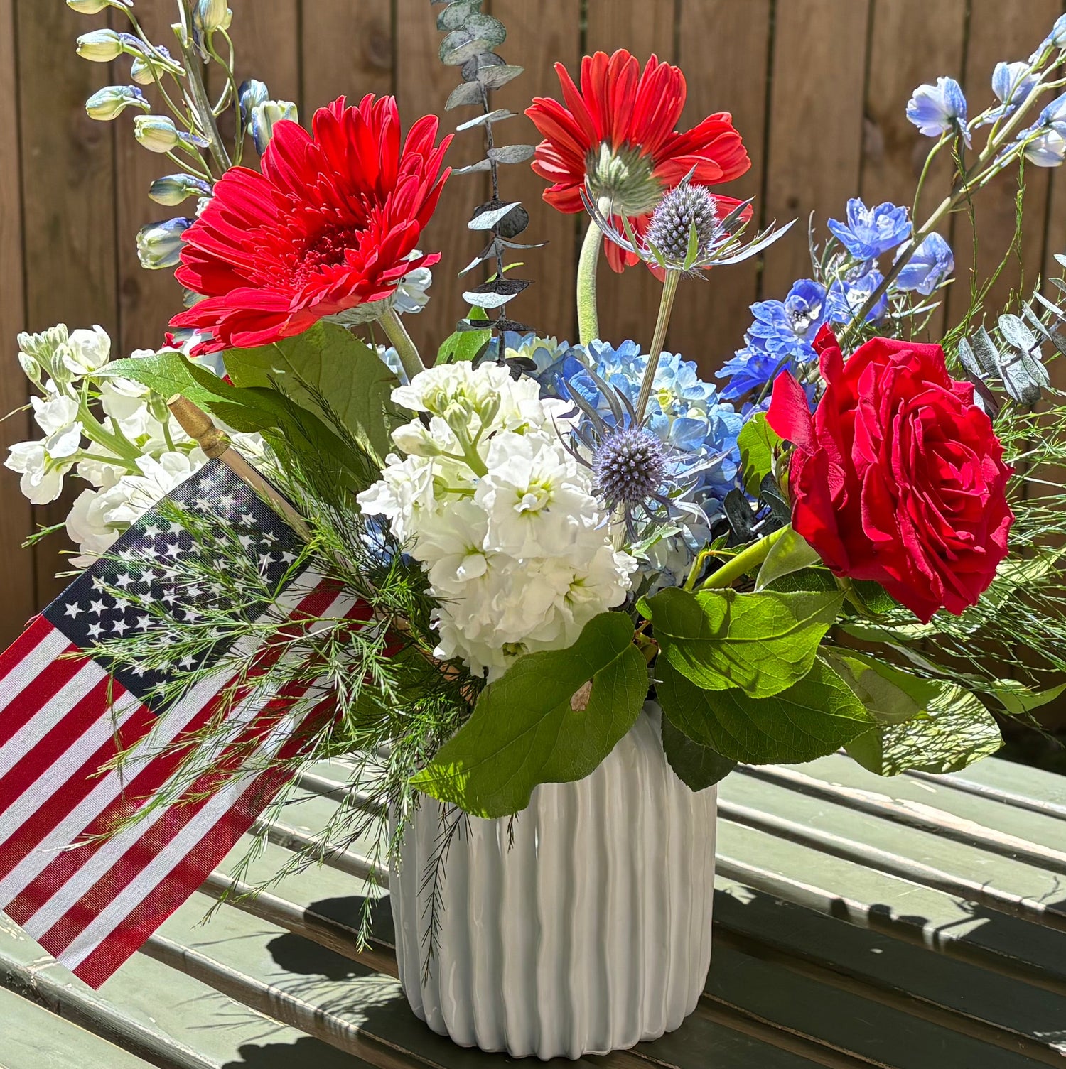 Floral arrangement with American flag in a vase on a wooden table outdoors.