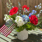 Colorful flower arrangement on a wooden deck with a chair and American flag in the background.