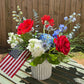 Bouquet of red, white, and blue flowers with an American flag on a wooden surface.