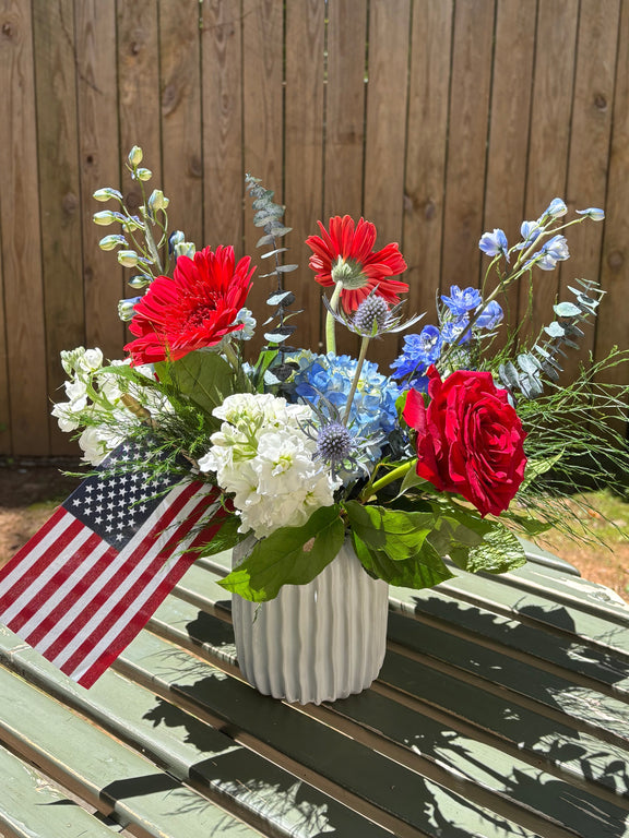 Bouquet of red, white, and blue flowers with an American flag on a wooden surface.