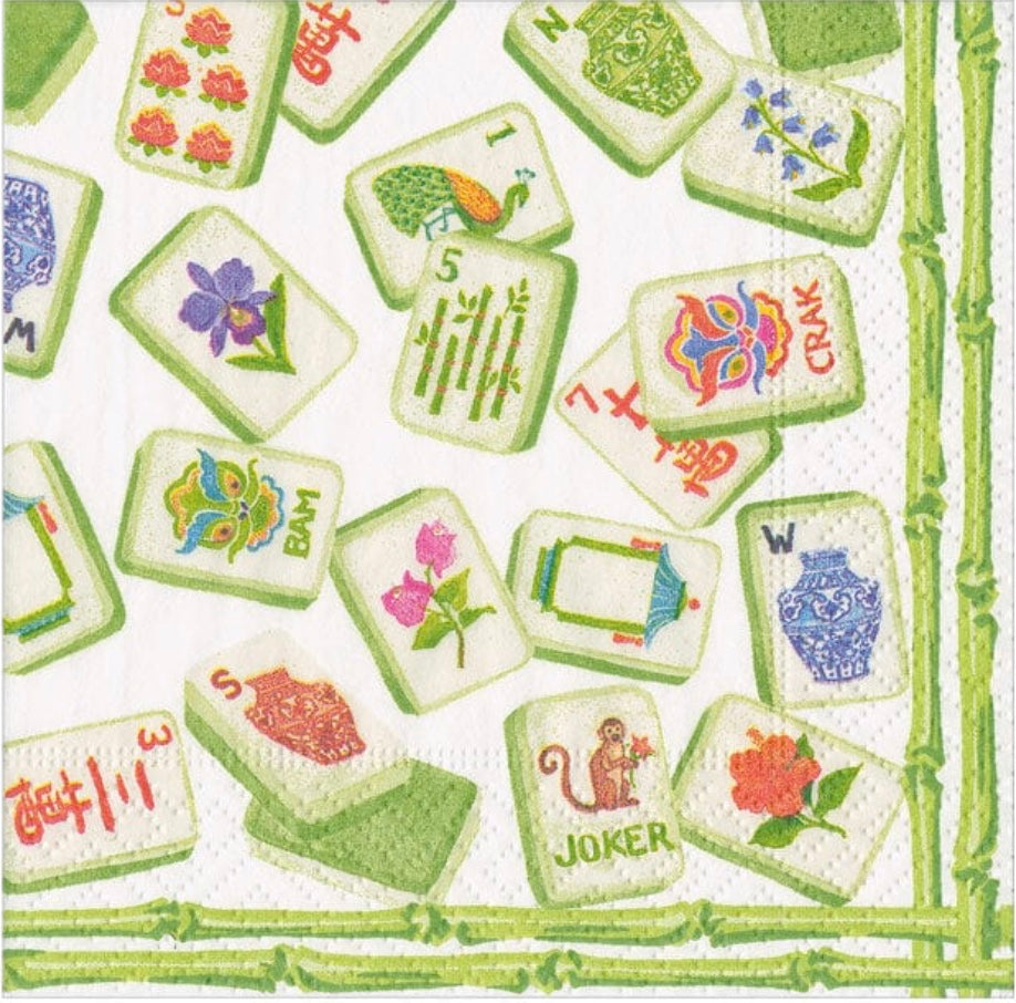 Caspari cocktail napkins featuring green borders with colorful illustrations of flowers, butterflies, playing cards, and botanical motifs on cream background