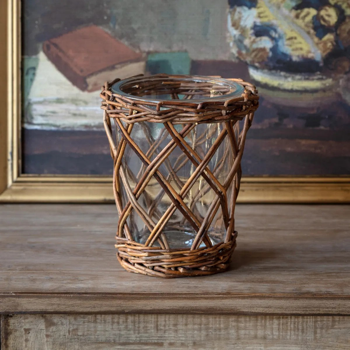 Woven rattan and glass candle holder with diagonal lattice pattern, warm brown finish, cylindrical shape.