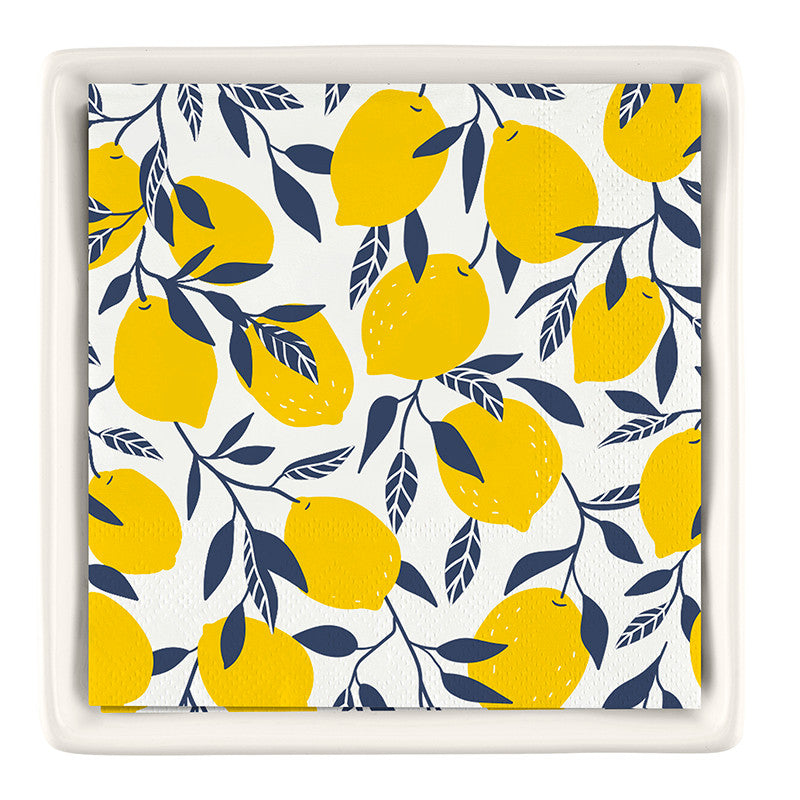 Ceramic napkin tray with white rim, featuring a lemon-print napkin insert with yellow lemons and navy foliage on cream background.