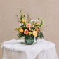 A vibrant medley of buttery yellow, rich peach, and crisp white blossoms bursts with life in a charming scalloped vase. Named for a quaint south Georgia town renowned for its Old South Day food, arts and crafts festival.