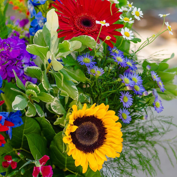 Bouquet of flowers with a sunflower and red gerbera daisy in a natural setting.