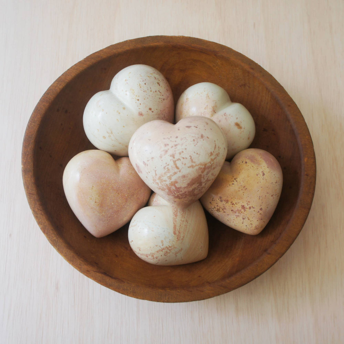 Hand-carved soapstone hearts in cream, tan, and beige tones with natural stone variations, arranged in a shallow wooden bowl.