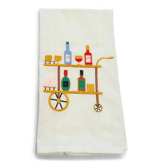 White flour sack towel with embroidered bar cart design featuring shelves of bottles, glasses, and barware in blue, red, green, and gold