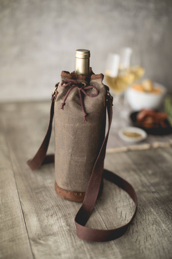 Taupe waxed canvas wine tote bag with burgundy drawstring and shoulder strap, holding wine bottle on wooden table