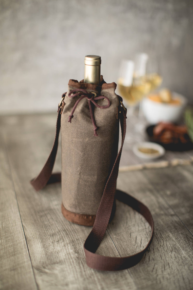 Taupe waxed canvas wine tote bag with burgundy drawstring and shoulder strap, holding wine bottle on wooden table