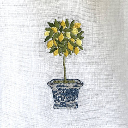 White linen kitchen towel with embroidered lemon topiary in yellow and green, set in a blue decorative pot.