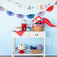 Colorful "USA" felt pennant banner with red, white, and purple letters strung across a light blue wall above a white shelf display with patriotic decorations.