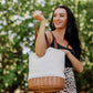 Cream canvas and woven willow Pico insulated basket tote with burgundy leather handles, held outdoors
