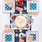Red, white, and blue star paper cups with checkered napkins and strawberries arranged on patriotic 4th of July party table.
