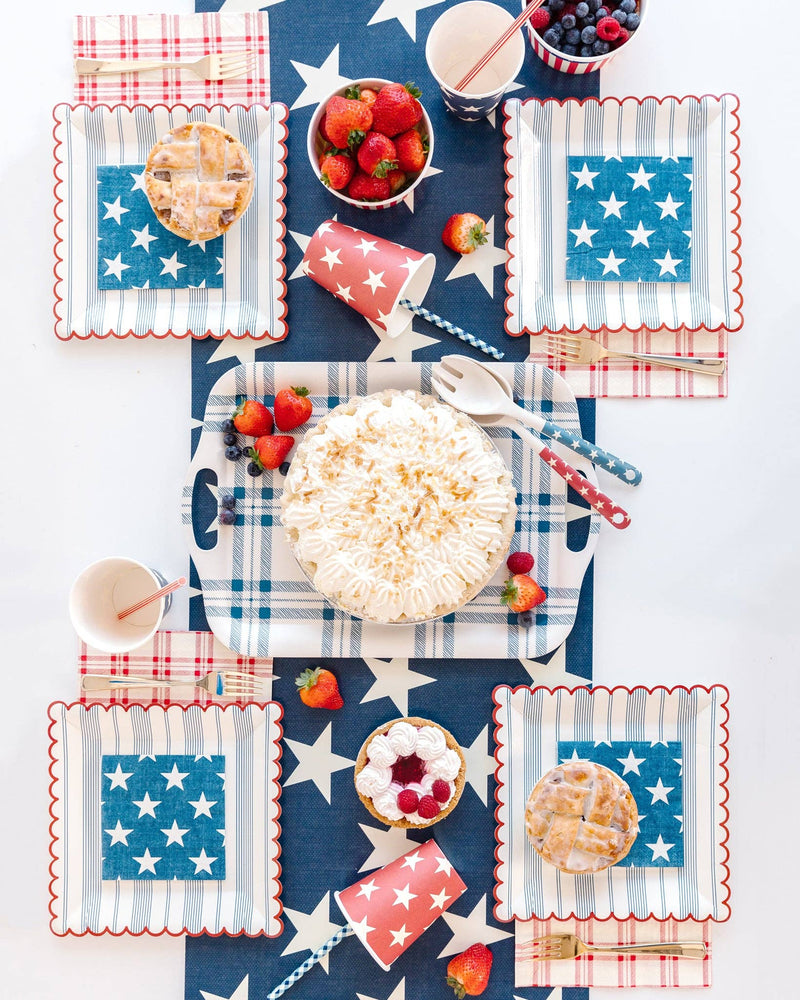 Red, white, and blue star paper cups with checkered napkins and strawberries arranged on patriotic 4th of July party table.