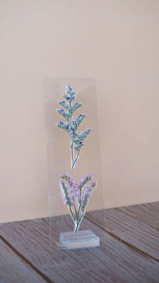 Clear resin bookmark with pressed blue forget-me-nots and lavender flowers in botanical design on acrylic display stand.