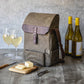 Tan canvas wine tote with burgundy leather flap holding two wine bottles, displayed with glasses of white wine, cheese board, and corkscrew