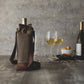 Tan distressed waxed canvas wine tote with burgundy handles and drawstring closure, holding a wine bottle beside wine glasses on wooden surface