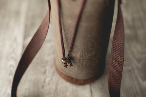 Distressed waxed canvas wine tote with burgundy fabric handles and metal toggle closure at bag opening