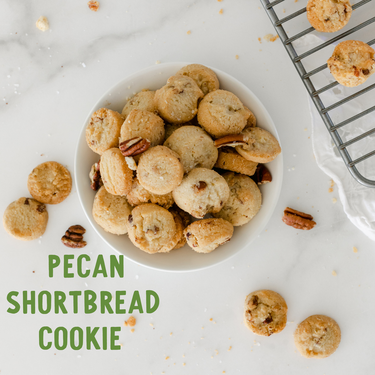 Golden pecan shortbread cookies with pecans in a white bowl on marble, surrounded by scattered cookies and cooling rack.