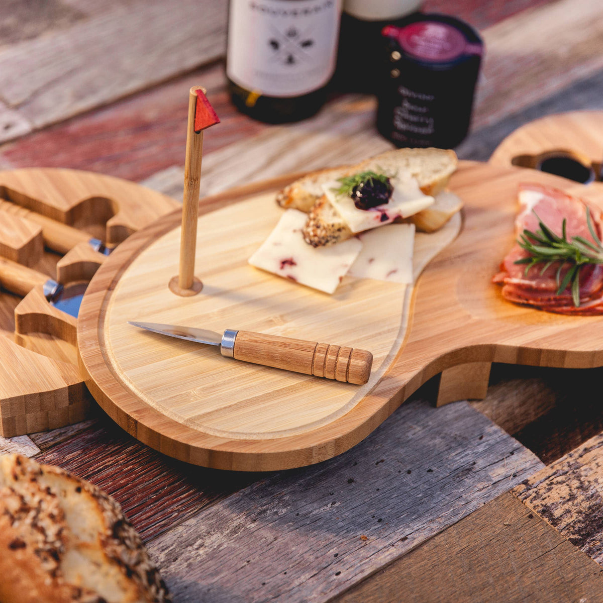 Bamboo golf club-shaped cheese board with red flag marker, swing-out drawers holding stainless steel utensils, styled with cured meats, cheese, and crackers on wooden surface