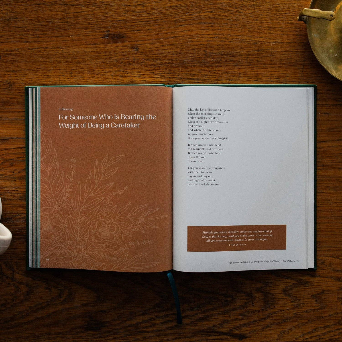 Open hardcover devotional book with rust-toned left page and cream right page displaying prayers and scripture, botanical illustration on cover.