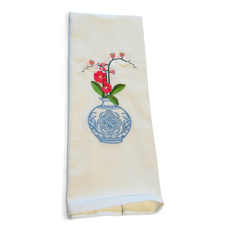 White cotton dish towel with embroidered red flowers in decorative blue vase and green leaves