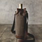 Tan waxed canvas wine bottle carrier with burgundy drawstring closure and adjustable shoulder strap, holding a wine bottle.