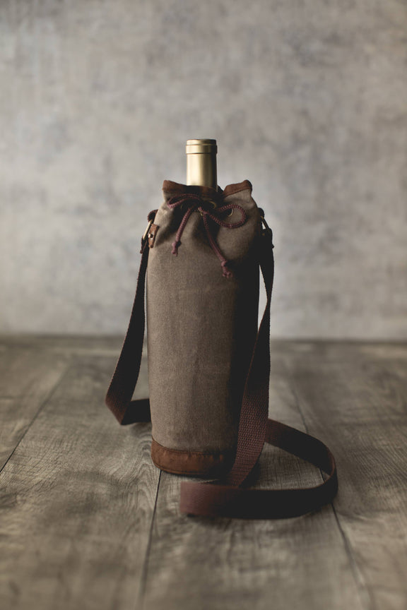 Tan waxed canvas wine bottle carrier with burgundy drawstring closure and adjustable shoulder strap, holding a wine bottle.
