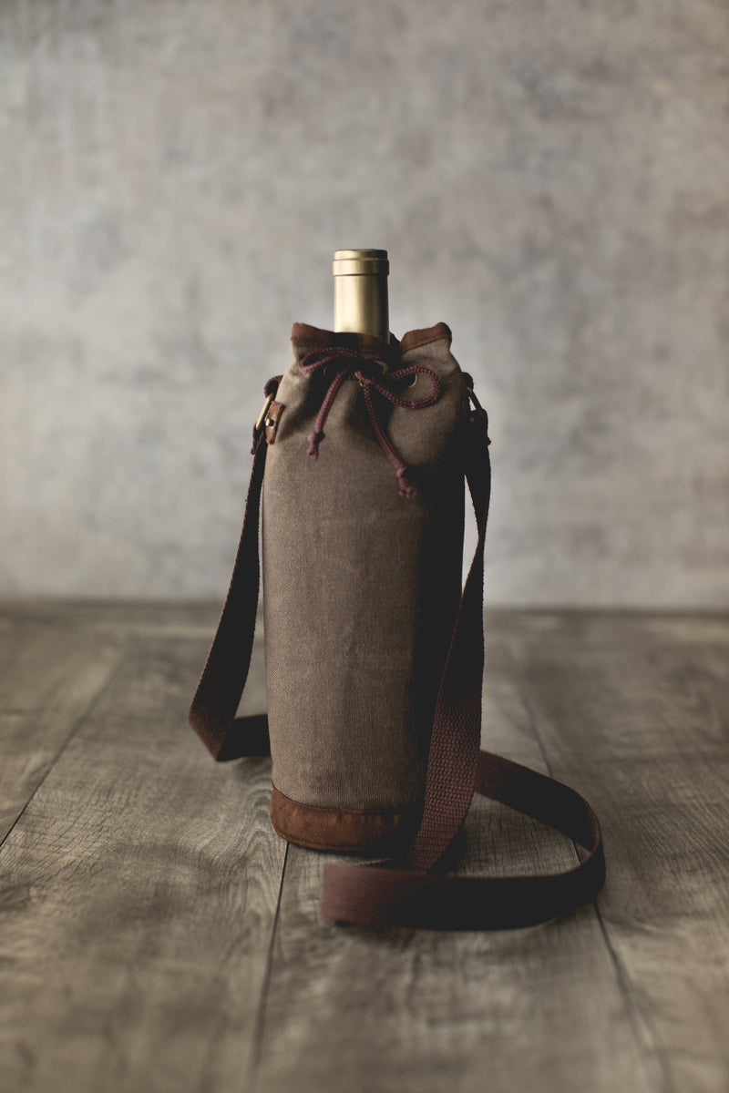Tan waxed canvas wine bottle carrier with burgundy drawstring closure and adjustable shoulder strap, holding a wine bottle.