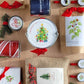 Garden in a Bag paperwhite gift set flat-lay showing seed packets, holiday-printed metal tins with ribbon bows, botanical illustrations, and festive red plaid accents on kraft and burlap