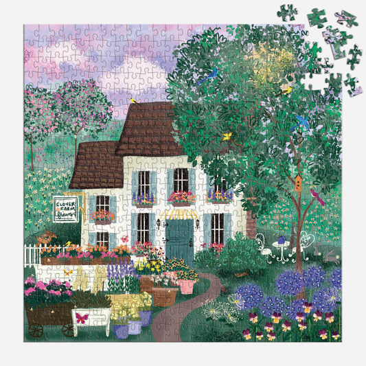 Jigsaw puzzle depicting cream cottage with brown roof nestled in lush garden, colorful blooms and climbing vines, loose pieces scattered