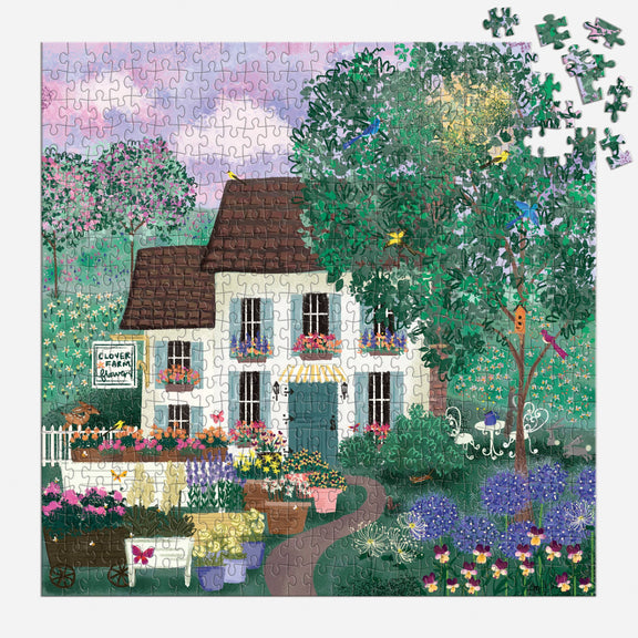 Jigsaw puzzle depicting cream cottage with brown roof nestled in lush garden, colorful blooms and climbing vines, loose pieces scattered