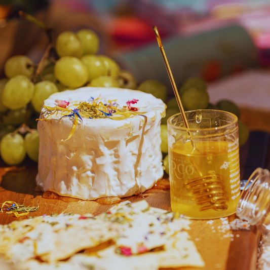Dried edible flower petals scattered on a white dish with fresh green grapes and golden honey garnish