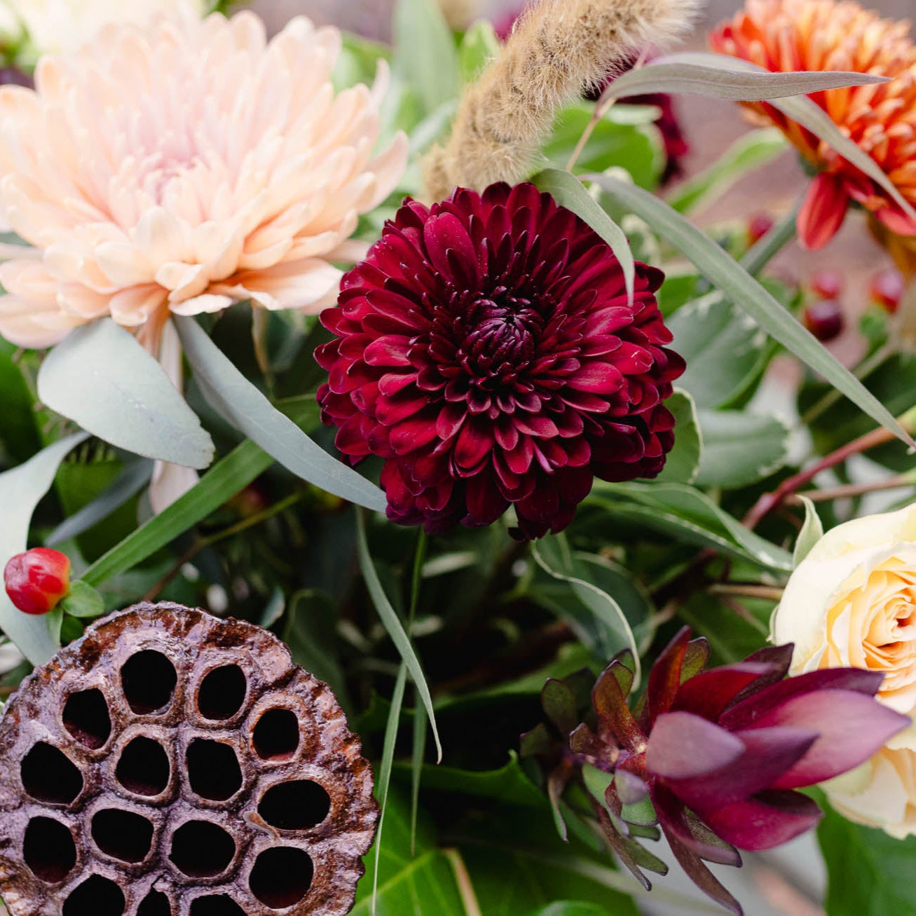 Close-up of a vibrant floral arrangement with a focus on a red flower and lotus seed pod.