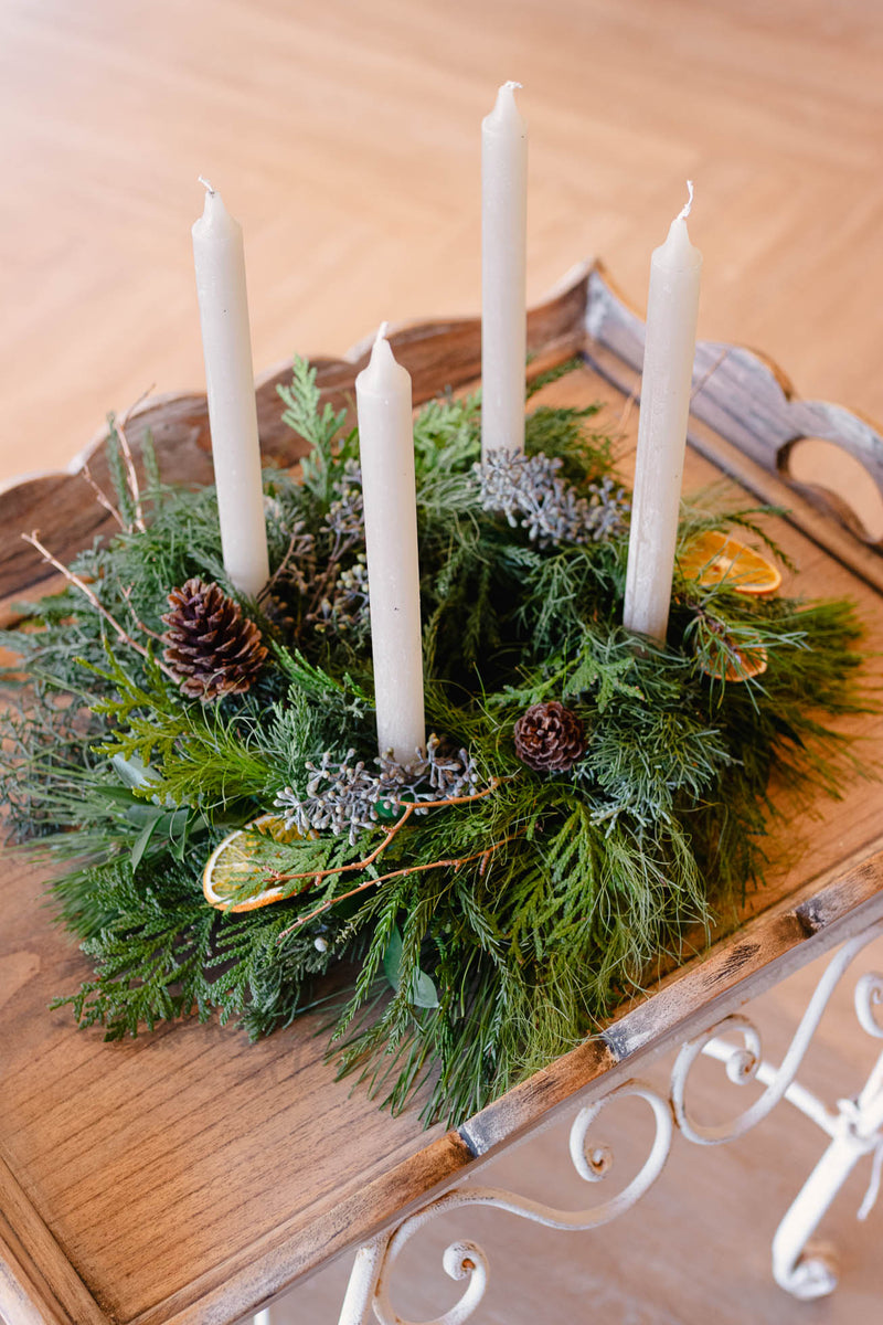 Decorative arrangement with candles and greenery on a wooden surface