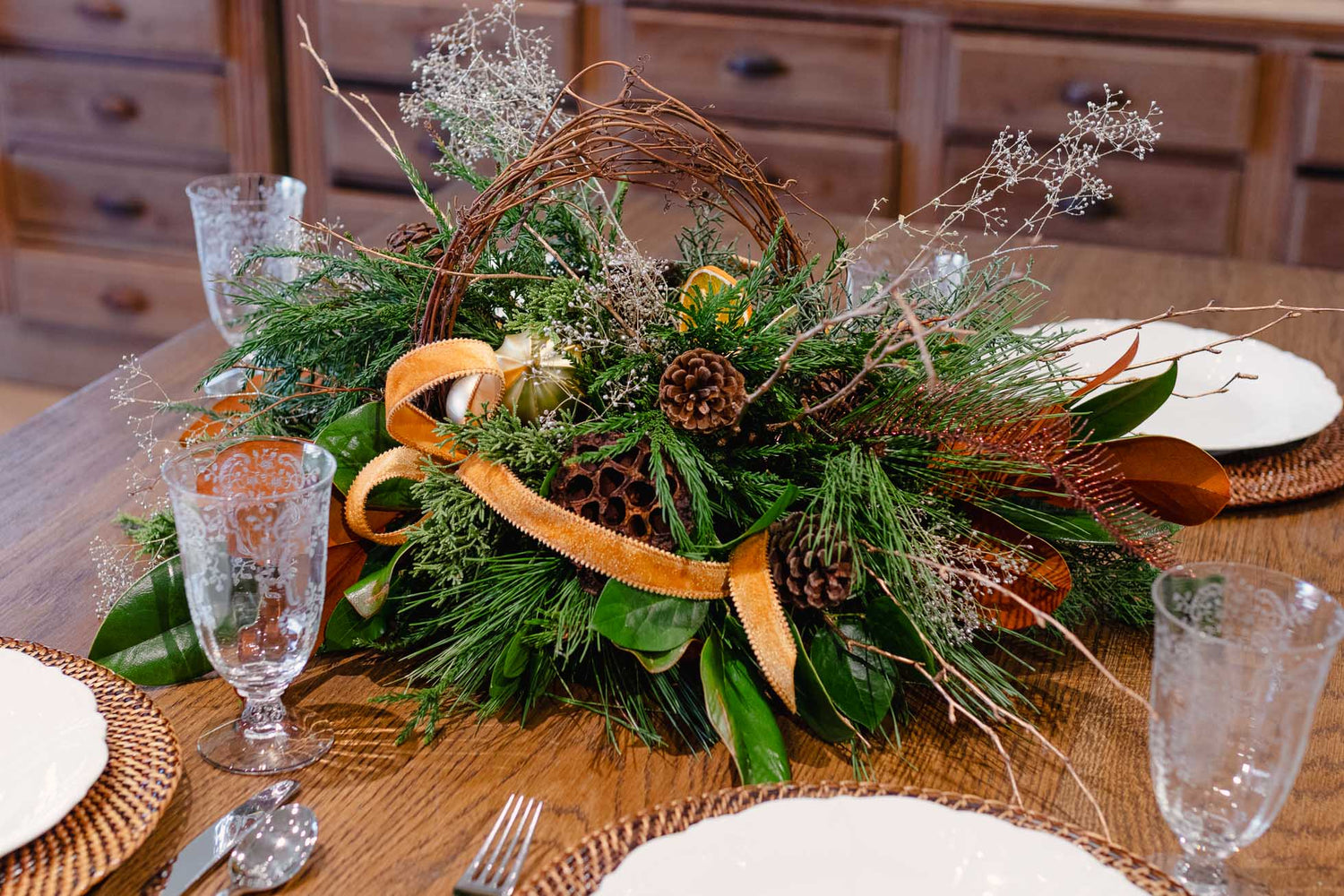 Decorative table centerpiece with greenery, ribbons, and pinecones on a wooden table.