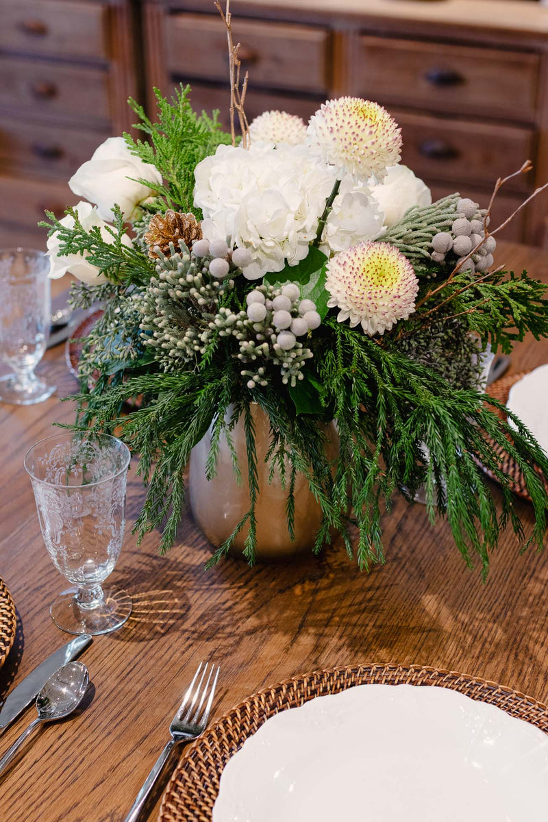 Floral arrangement on a wooden table with glasses and cutlery