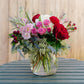 Bouquet of red, pink, and white flowers in a clear vase on a wooden surface.