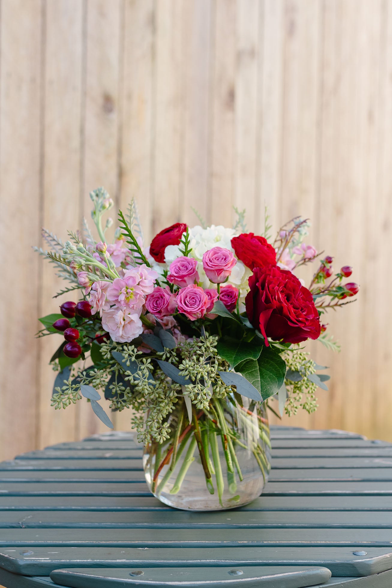 Bouquet of red, pink, and white flowers in a clear vase on a wooden surface.