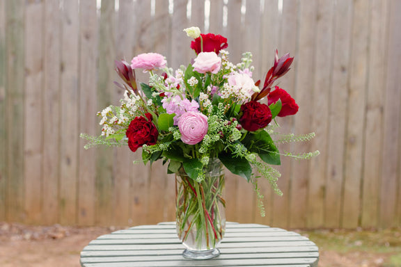 Bouquet of flowers in a vase on a wooden table with a wooden fence background