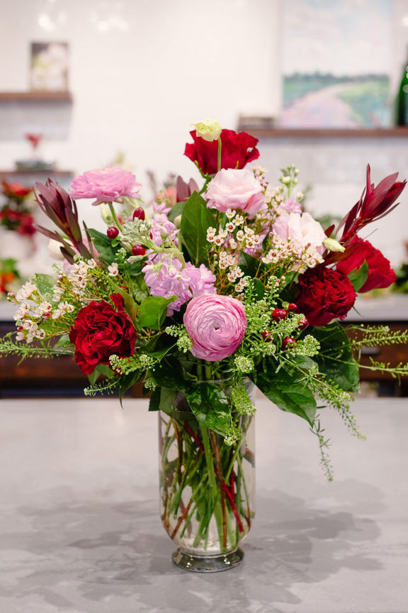 Bouquet of red and pink flowers in a clear vase on a marble surface.