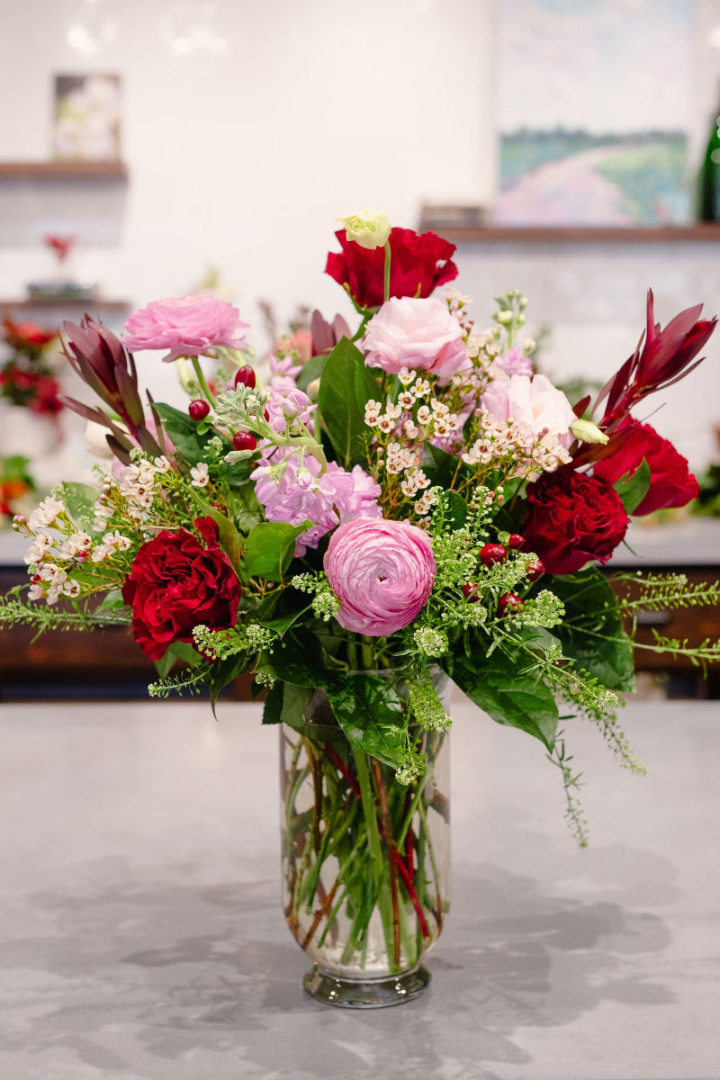 Bouquet of red and pink flowers in a clear vase on a marble surface.