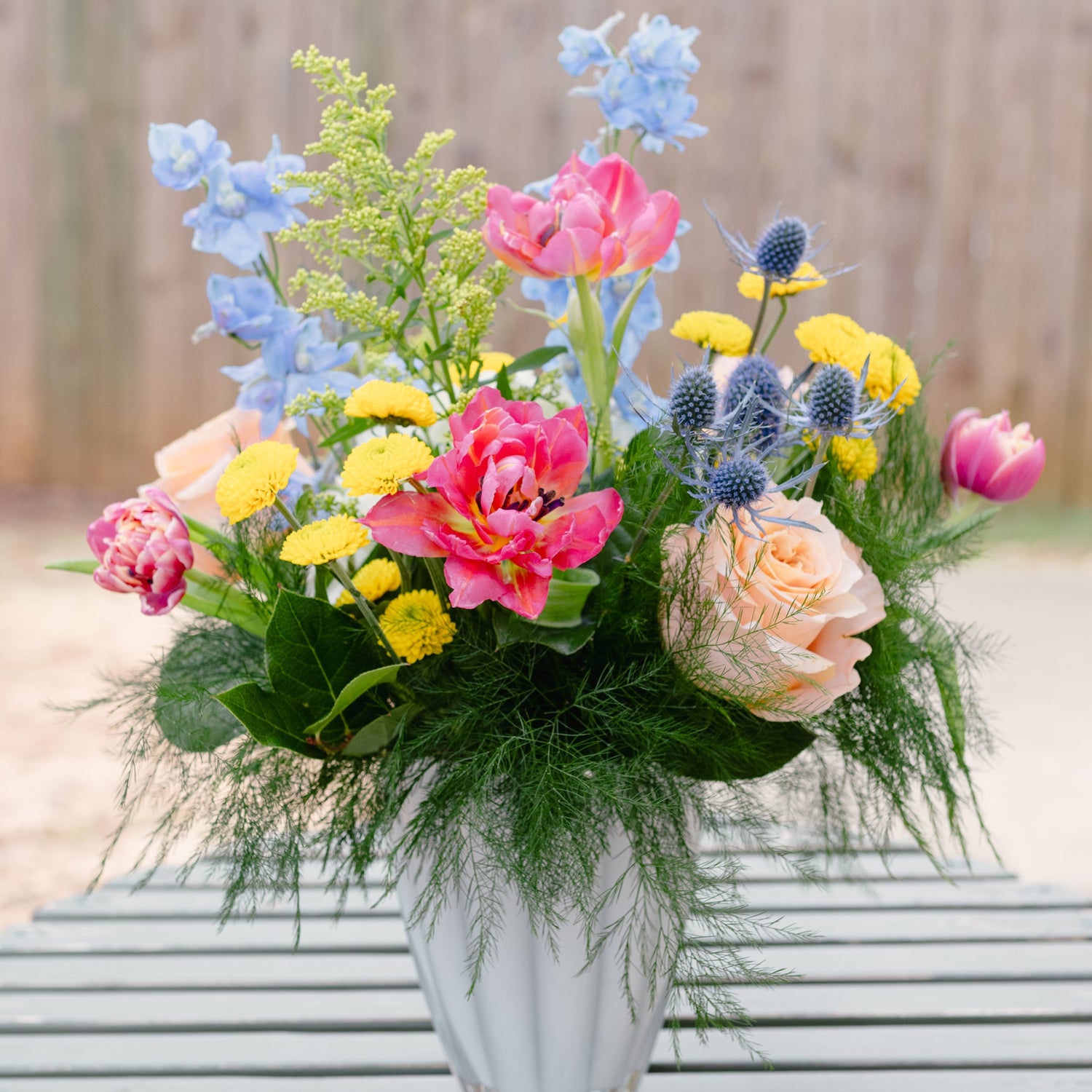 Colorful flower arrangement in a clear vase on a table outdoors.